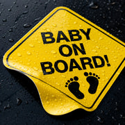 Close-up of a yellow Baby on Board vinyl decal with water beading on the glossy surface.
