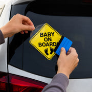 Hands applying a Baby on Board vinyl decal to a rear vehicle window using a blue squeegee.