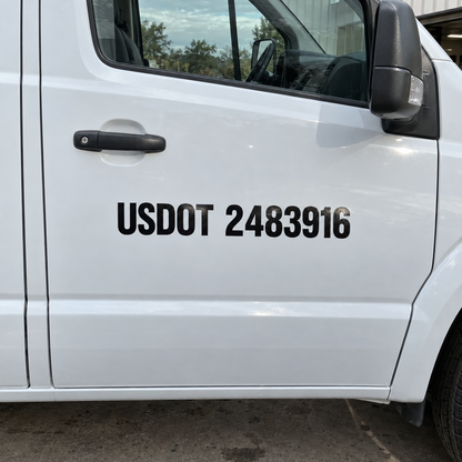 Black reflective USDOT 2483916 lettering sits clear of the handle and seam on a white work van’s passenger door.