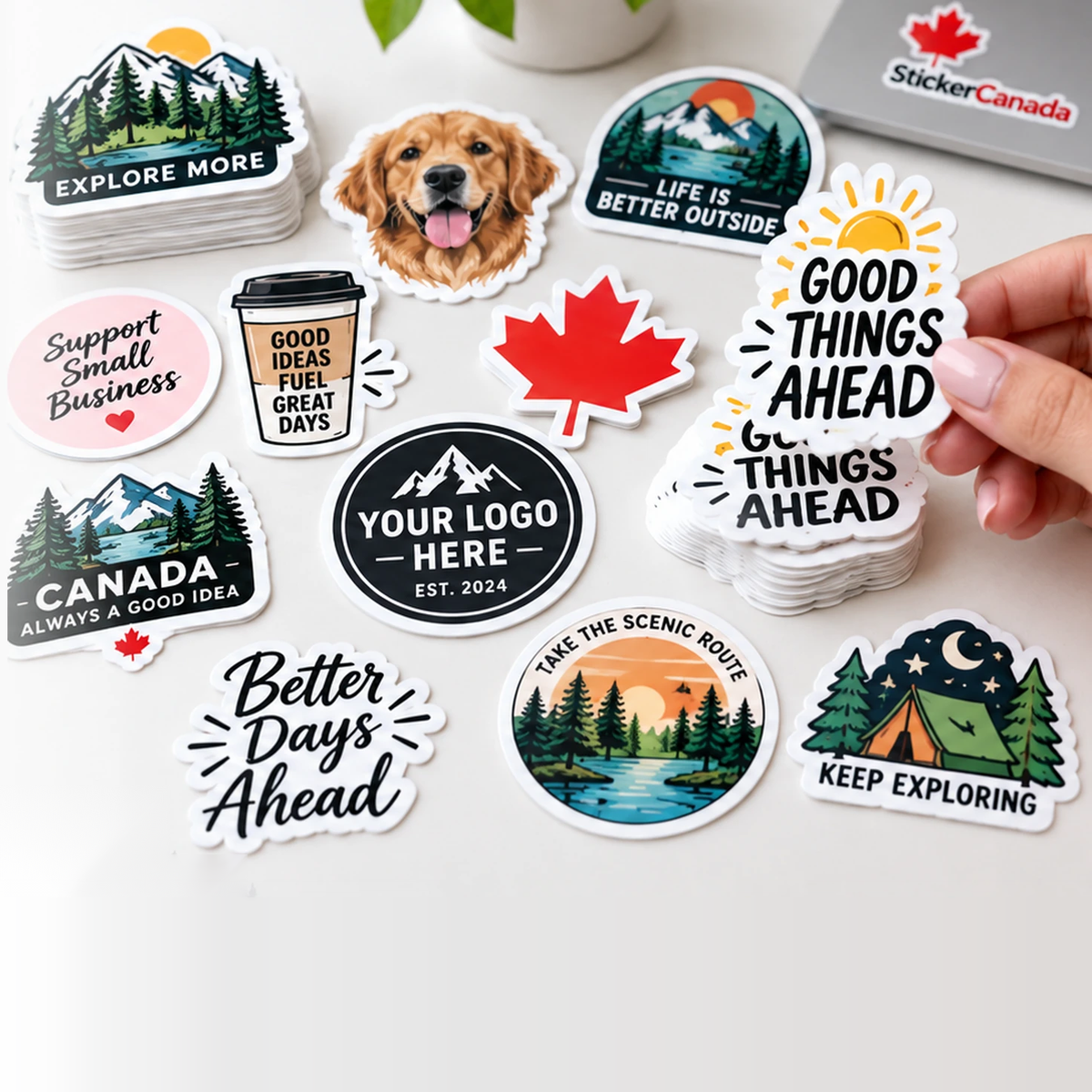 Real printed custom die-cut vinyl stickers in everyday outdoor lifescene style: an assorted stack on a work desk with one sticker being lifted from the stack — printed in Ontario, made for outdoor use