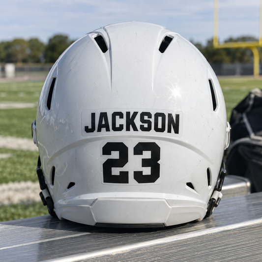 Jackson name and number 23 stickers on the back of a football helmet on a field bench.