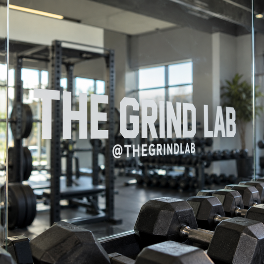 White The Grind Lab and @THEGRINDLAB vinyl lettering on a mirror with weights reflected.