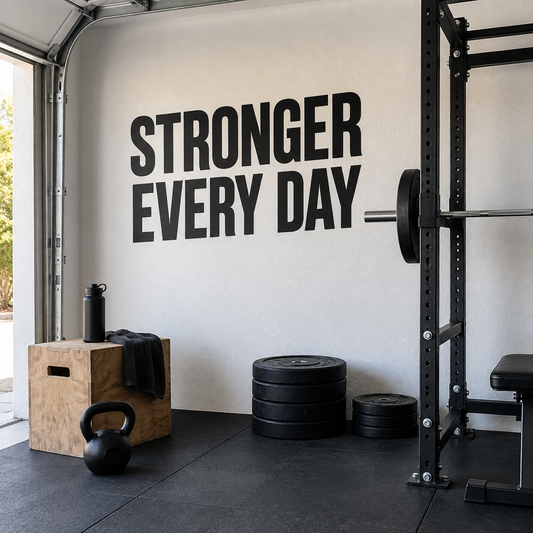 Black Stronger Every Day vinyl lettering on a white garage wall beside a squat rack.