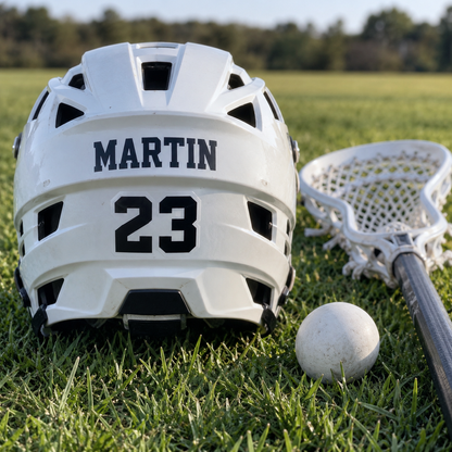 Martin name and number 23 stickers on a lacrosse helmet beside a stick and ball on grass.