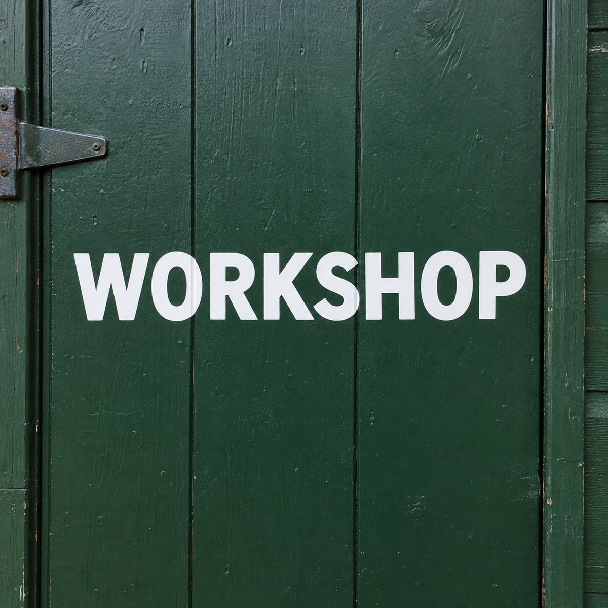 White vinyl capitals spelling WORKSHOP applied across a dark green painted shed door in daylight. - Vinyl Alphabet Letters — A-Z 0-9 Kit