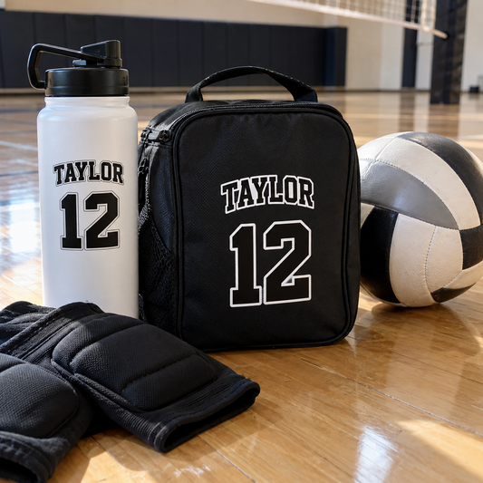 Taylor name and number 12 stickers on a water bottle and knee-pad bag beside a volleyball.